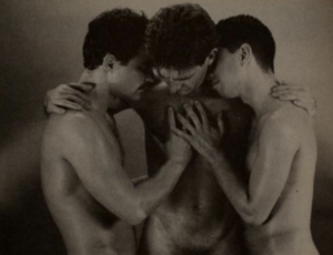 Photo of three shirtless men embracing.